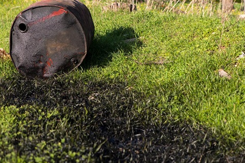 An oil can that is tipped over. Oil is spilled all over the grass swale area.