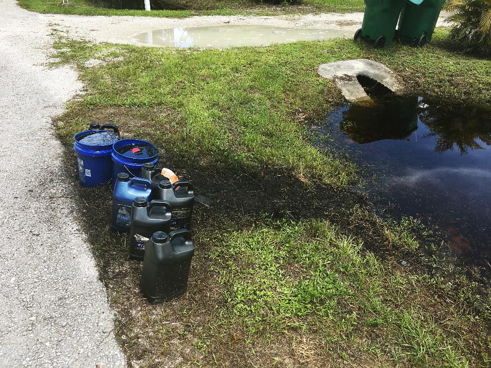 Oil containers placed at the end of a driveway are leaking oil into the stormwater swale. 